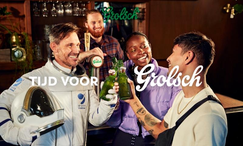 Astronaut en twee andere mensen proosten met Grolsch beugels voor een bar